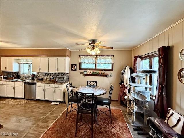 kitchen featuring stainless steel dishwasher, healthy amount of natural light, ornamental molding, dark countertops, and a ceiling fan