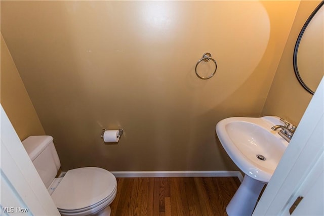 half bathroom with wood finished floors, toilet, and baseboards