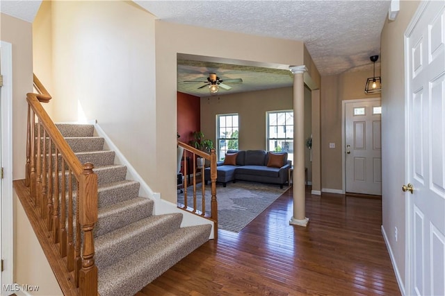 foyer with wood finished floors, a ceiling fan, stairs, a textured ceiling, and ornate columns