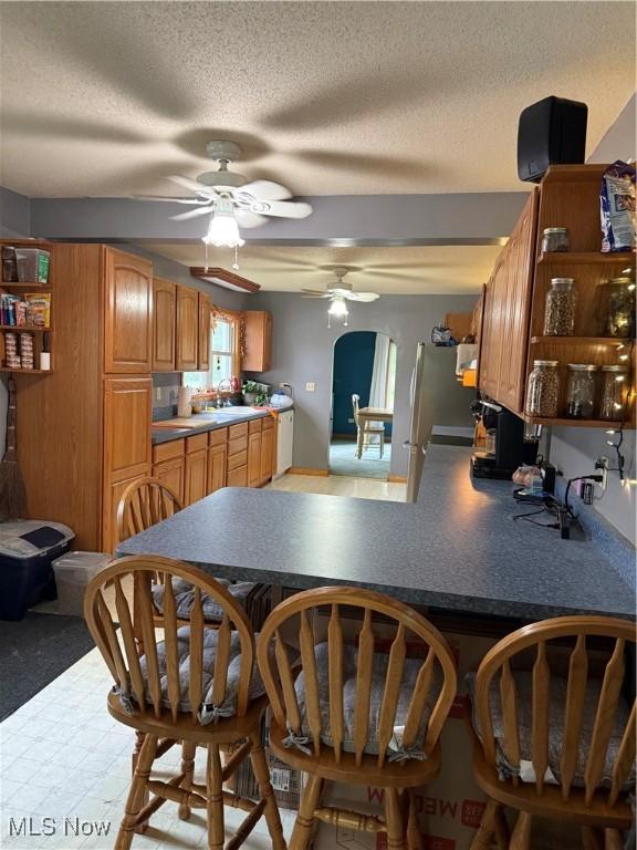 kitchen featuring open shelves, ceiling fan, a textured ceiling, a peninsula, and a sink
