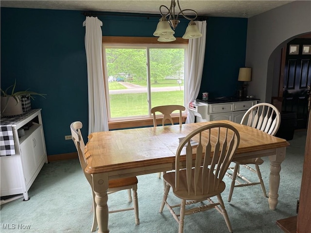 dining space featuring arched walkways, light colored carpet, and a chandelier