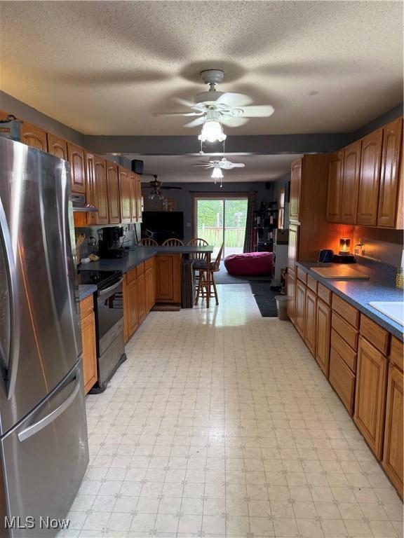 kitchen featuring freestanding refrigerator, range with electric cooktop, ceiling fan, a peninsula, and a textured ceiling