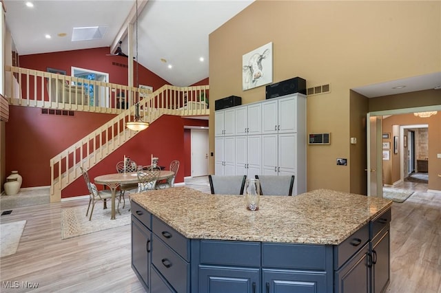 540 Bent Creek Oval, Aurora, OH 44202 - kitchen featuring high vaulted ceiling, blue cabinets, light wood-type flooring, light stone counters, and a center island