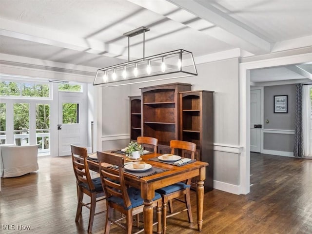 dining area featuring wood finished floors, a decorative wall, beamed ceiling, and wainscoting