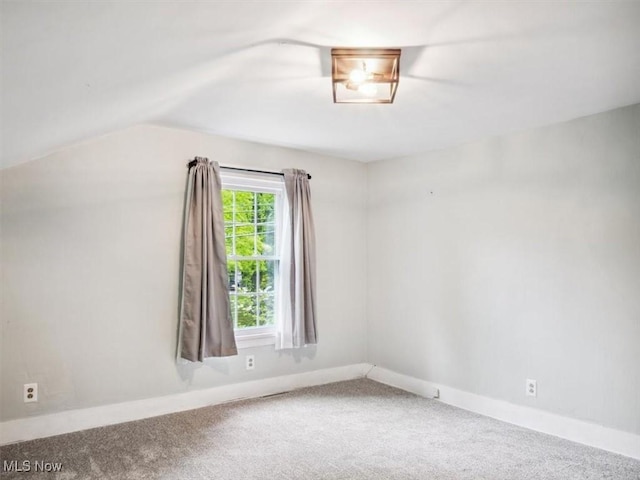 spare room featuring carpet, lofted ceiling, and baseboards
