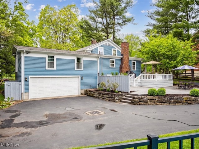 view of front of house with driveway, an attached garage, a chimney, and a deck