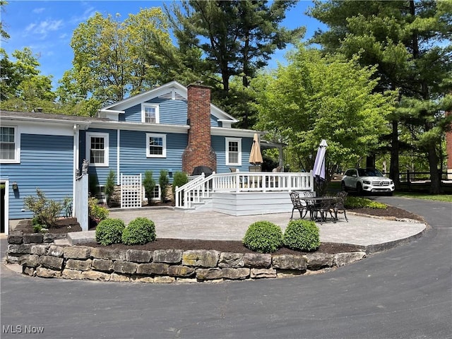 rear view of property with a chimney, a deck, and a patio