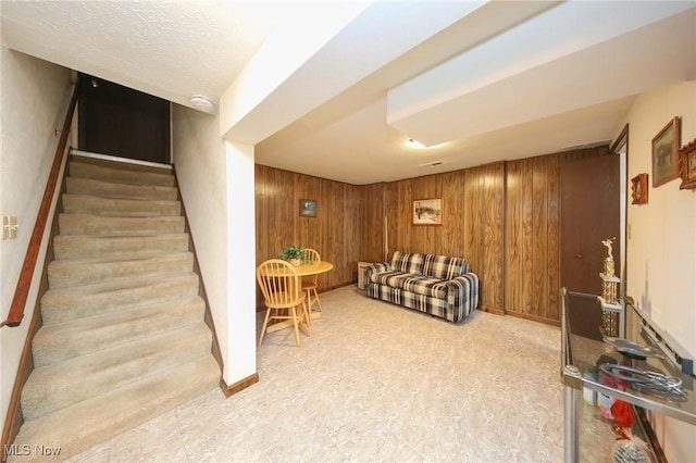 living area featuring wood walls, stairway, baseboards, and carpet floors