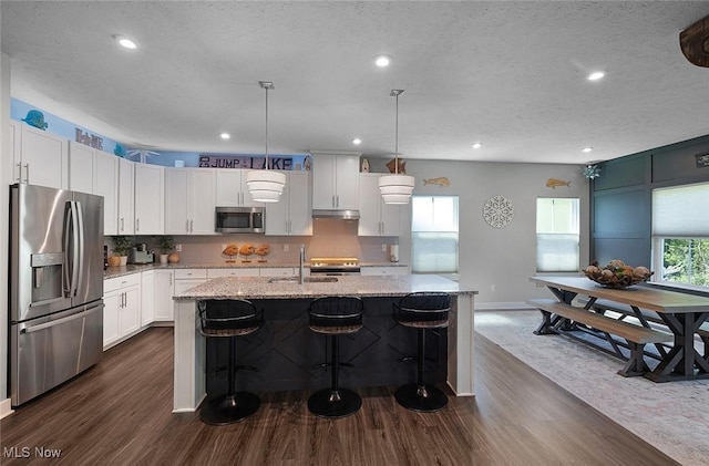 kitchen featuring appliances with stainless steel finishes, a sink, dark wood-style flooring, light stone countertops, and baseboards