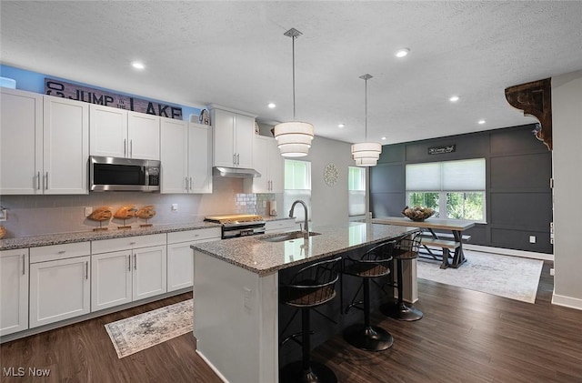 kitchen with stainless steel appliances, a sink, dark wood finished floors, decorative backsplash, and white cabinetry