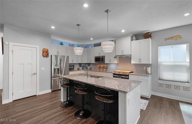 kitchen with stainless steel appliances, under cabinet range hood, a sink, dark wood-style floors, and baseboards