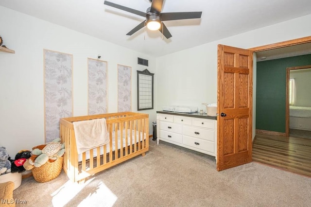 bedroom featuring a nursery area, light colored carpet, and a ceiling fan
