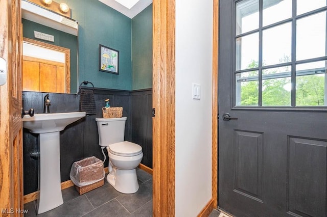 bathroom featuring toilet, tile patterned flooring, baseboards, and a wainscoted wall