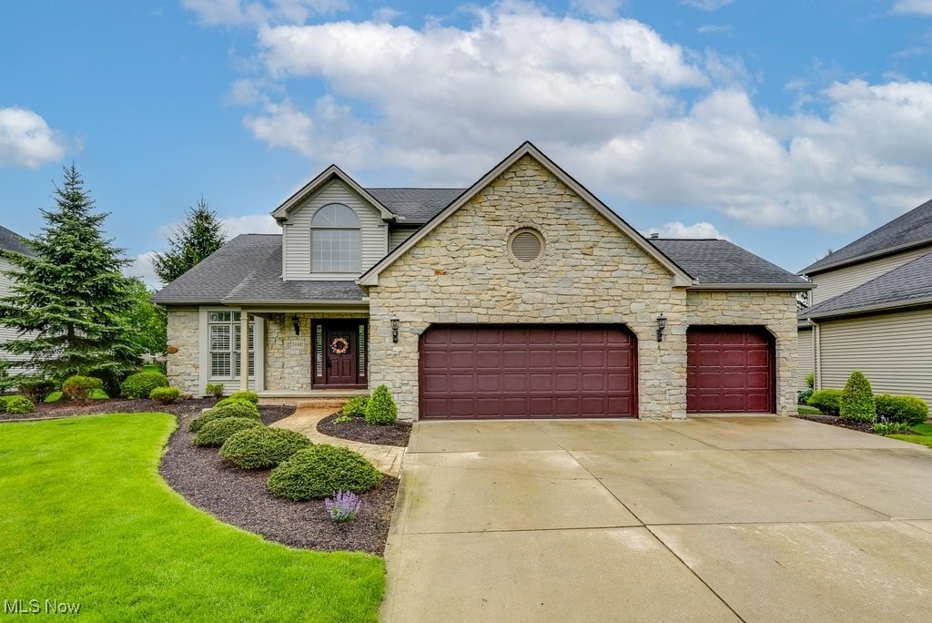 20481 Bradgate Ln, Strongsville, OH 44149 - view of front of property featuring stone siding, an attached garage, driveway, a front lawn, and roof with shingles