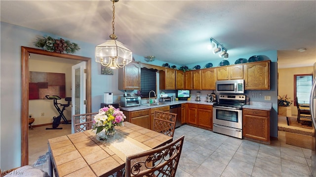 kitchen featuring stainless steel appliances, a chandelier, light countertops, brown cabinetry, and pendant lighting