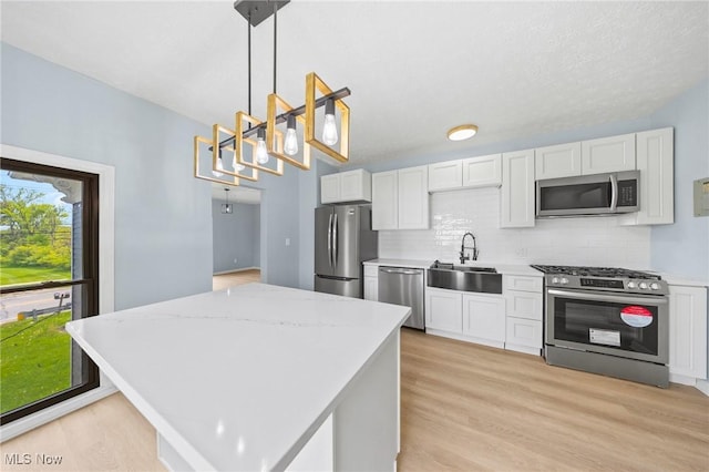 9324 Columbia Rd, Olmsted Falls, OH 44138 - kitchen featuring stainless steel appliances, a sink, light wood-style flooring, white cabinets, and decorative light fixtures