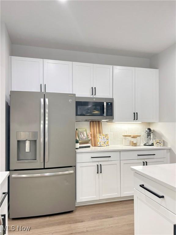 1810 Muirfield Ln, Painesville, OH 44077 - kitchen featuring stainless steel appliances, white cabinets, light countertops, light wood finished floors, and tasteful backsplash