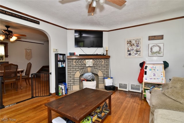 living area with ceiling fan, a textured ceiling, hardwood / wood-style floors, ornamental molding, and arched walkways