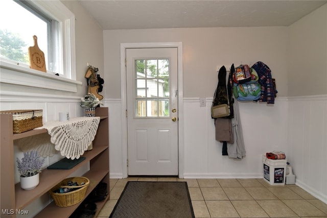 doorway to outside with light tile patterned floors, a wainscoted wall, and a decorative wall