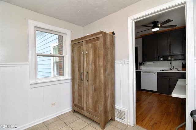 kitchen featuring white dishwasher, a sink, a ceiling fan, light countertops, and light tile patterned floors