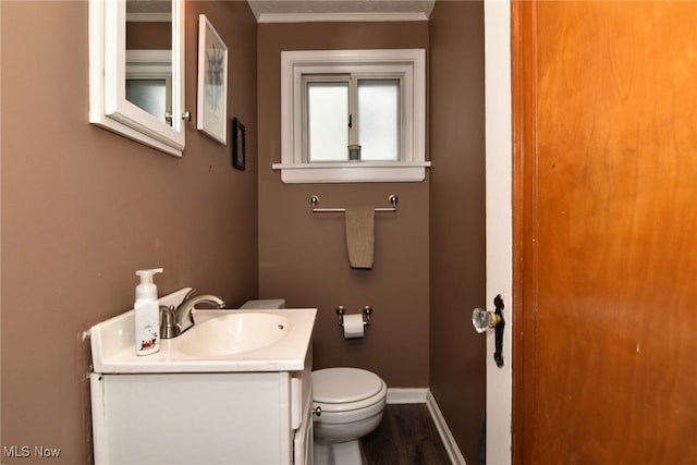 half bathroom with toilet, vanity, crown molding, wood finished floors, and baseboards