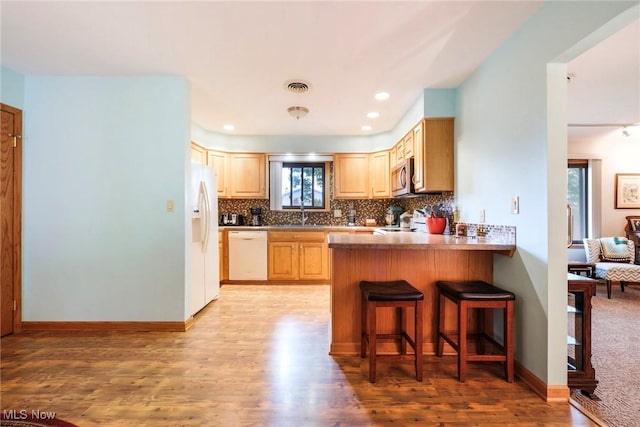 kitchen with white appliances, light wood-style flooring, a peninsula, light brown cabinets, and decorative backsplash