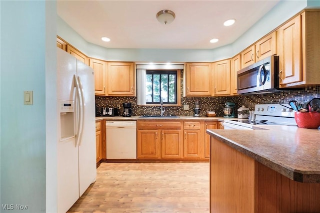 kitchen featuring white appliances, a sink, light wood-style floors, decorative backsplash, and a peninsula