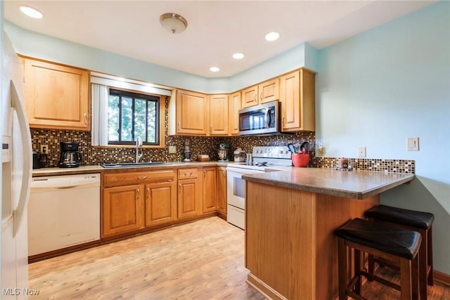 kitchen featuring white appliances, a sink, a peninsula, a kitchen bar, and light wood-style flooring