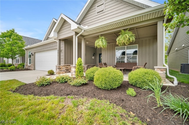 view of front of house featuring a porch, stone siding, an attached garage, board and batten siding, and concrete driveway
