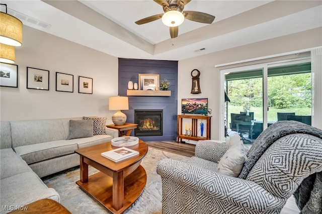 living room featuring a fireplace, a ceiling fan, and a tray ceiling