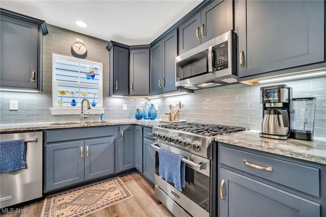 kitchen featuring stainless steel appliances, a sink, light stone counters, light wood-style floors, and backsplash