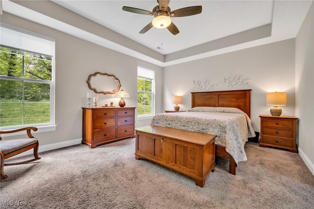 bedroom featuring light colored carpet, baseboards, a tray ceiling, and ceiling fan