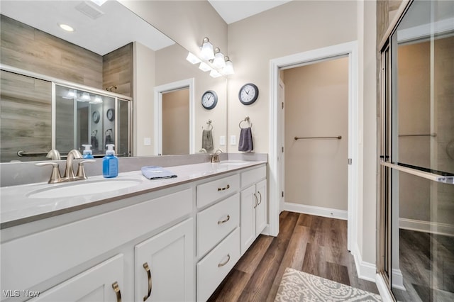 full bath with a shower stall, wood finished floors, double vanity, and baseboards