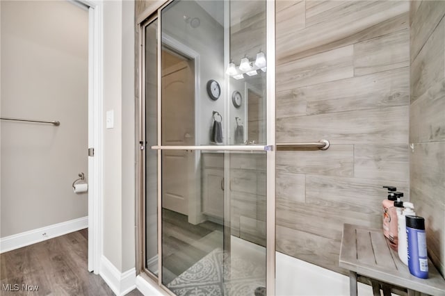 full bath featuring a shower stall, baseboards, and wood finished floors