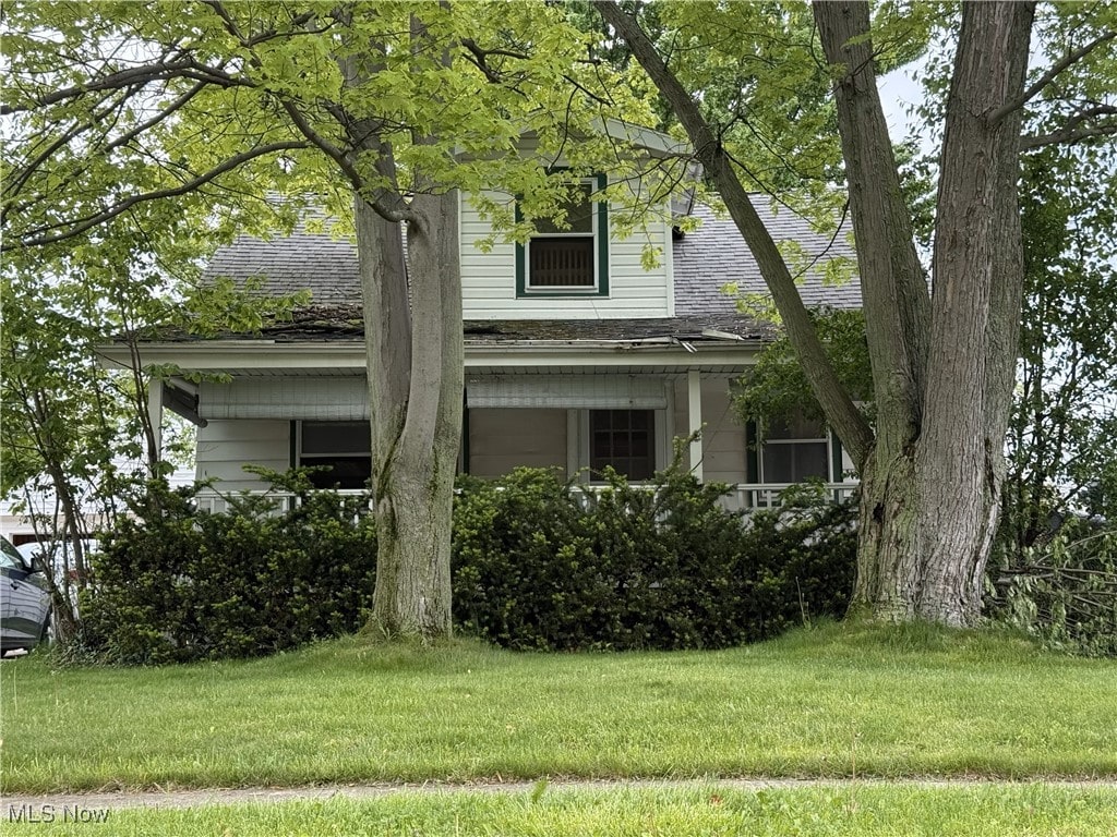 obstructed view of property featuring a front lawn and a shingled roof