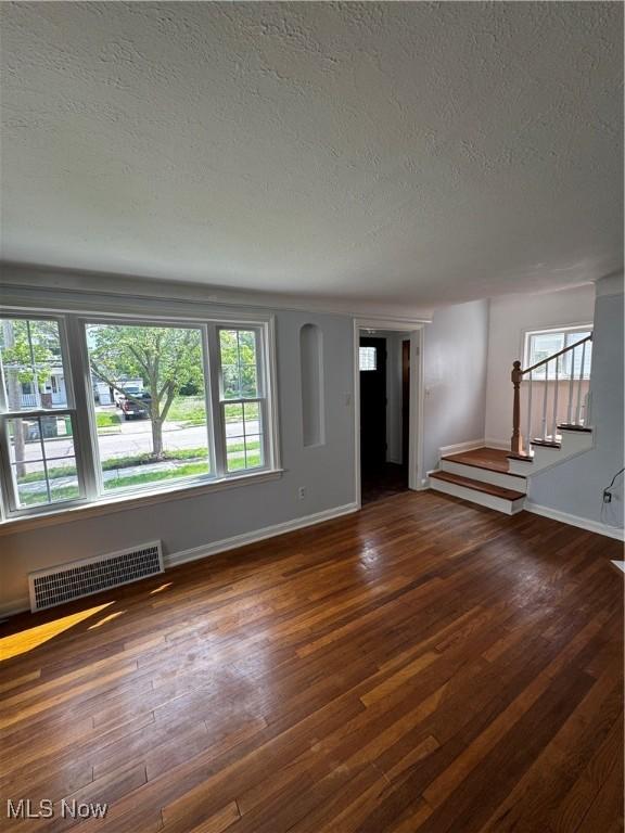 empty room featuring a textured ceiling, baseboards, stairway, and plenty of natural light