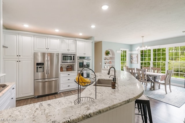 kitchen featuring appliances with stainless steel finishes, a sink, a chandelier, wood finished floors, and a breakfast bar