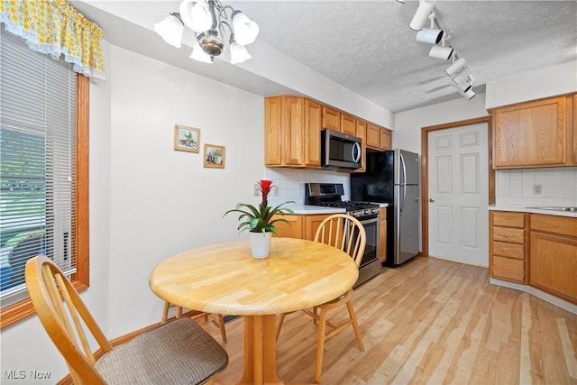 kitchen featuring stainless steel appliances, a chandelier, light wood finished floors, decorative backsplash, and light countertops