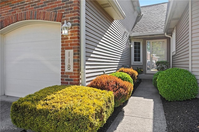 view of exterior entry featuring roof with shingles and brick siding