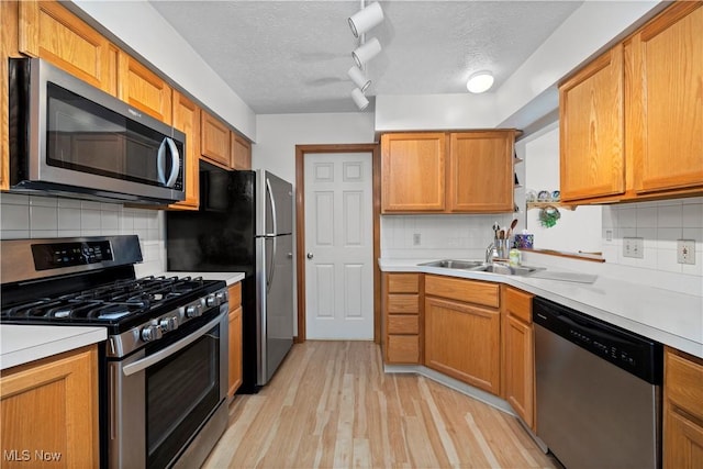kitchen with stainless steel appliances, a sink, a textured ceiling, and decorative backsplash