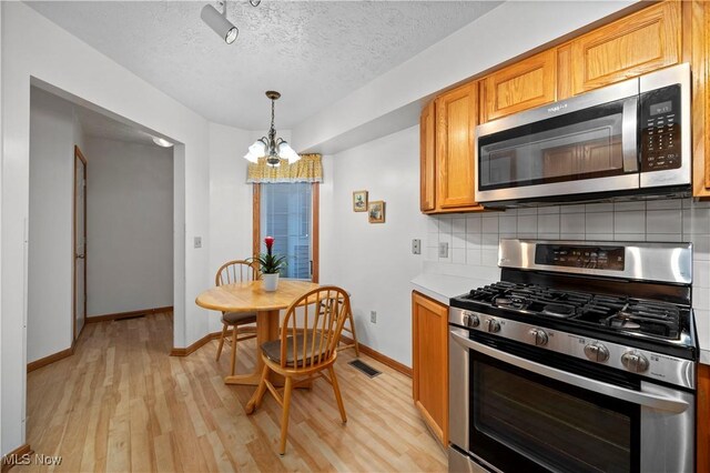 kitchen featuring appliances with stainless steel finishes, backsplash, light wood-style floors, light countertops, and a textured ceiling