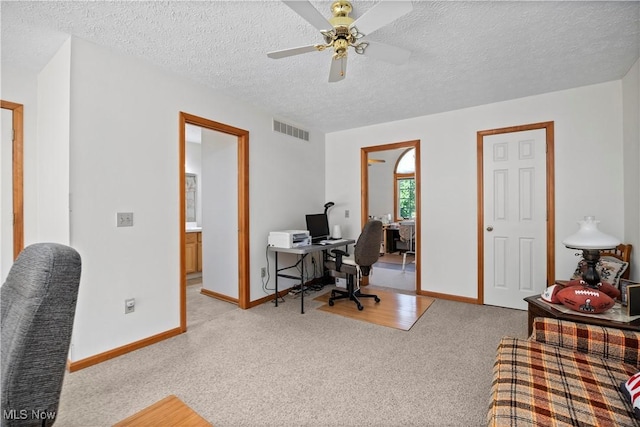 office space with light colored carpet, a ceiling fan, baseboards, and a textured ceiling