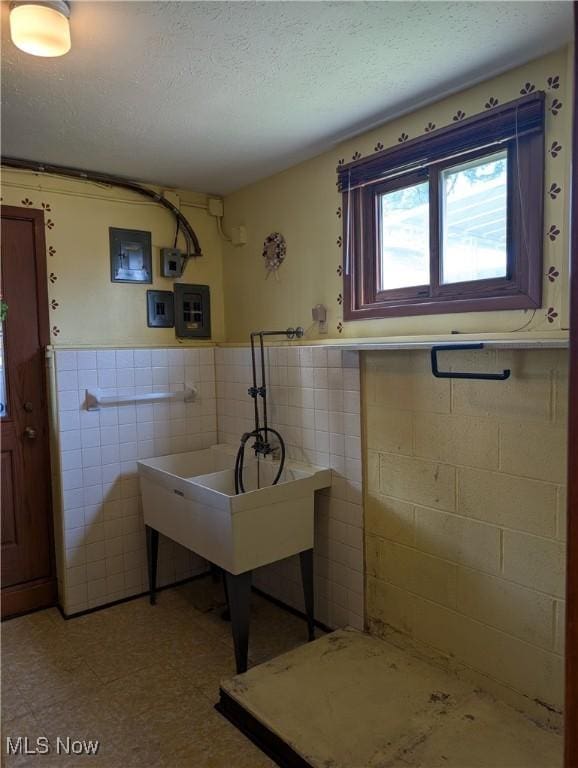 bathroom featuring tile patterned floors, tile walls, a textured ceiling, a wainscoted wall, and electric panel