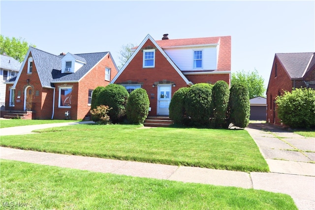 english style home with a front yard, brick siding, and a chimney