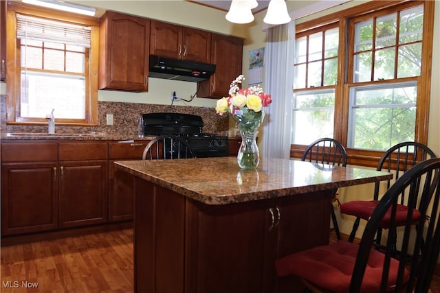 kitchen with under cabinet range hood, black range with gas stovetop, a sink, a breakfast bar area, and wood finished floors