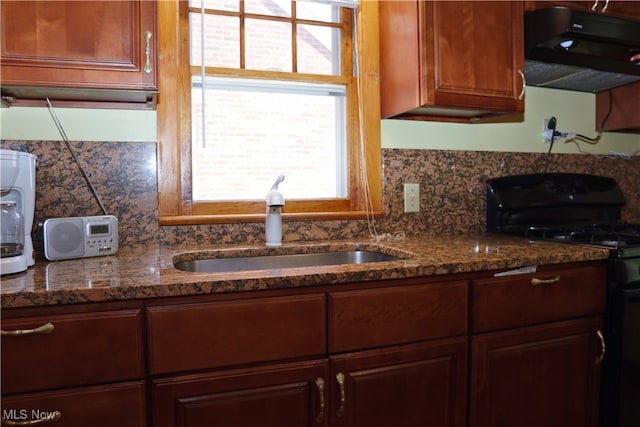 kitchen featuring black gas stove, exhaust hood, a sink, backsplash, and dark stone counters