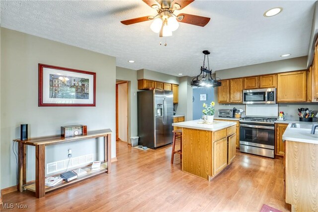 kitchen with appliances with stainless steel finishes, light countertops, a kitchen island, light wood-type flooring, and ceiling fan