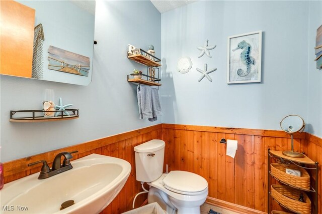 half bathroom featuring a sink, a wainscoted wall, wooden walls, and toilet