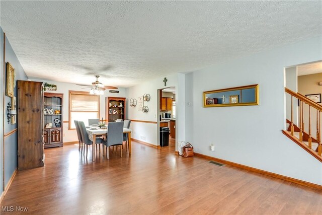 dining space with a textured ceiling, wood finished floors, ceiling fan, stairs, and baseboards
