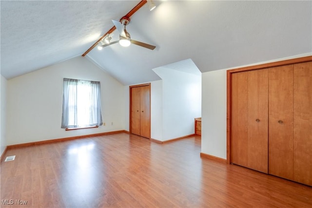 additional living space featuring light wood-style flooring, lofted ceiling, ceiling fan, baseboards, and a textured ceiling